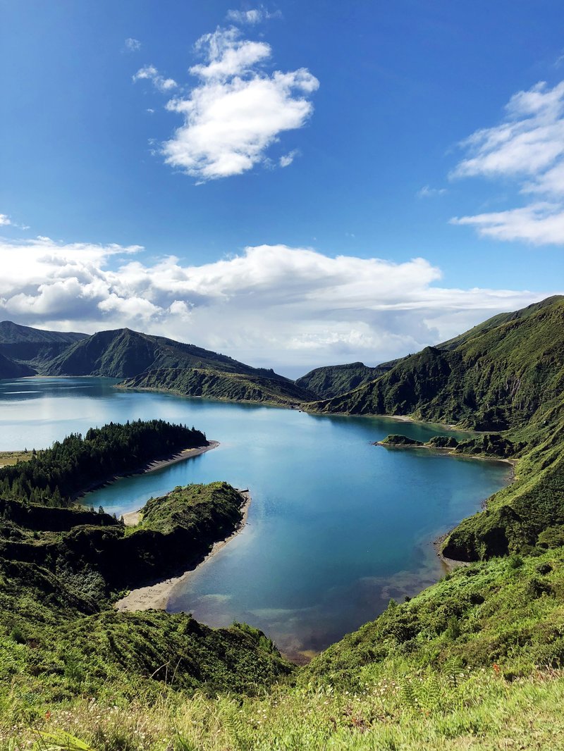 A crater lake set among green volcanic mountains under a blue sky, similar to Lagoa do Fogo