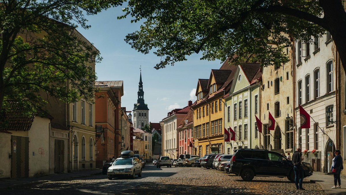 Cobbled street in Tallinn Old Town with parked cars and a church spire in the distance