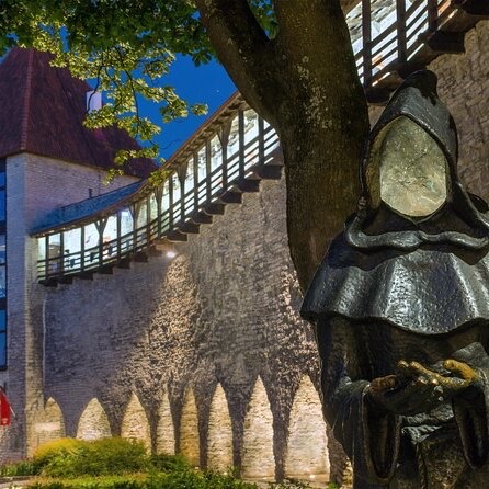Tallinn Old Town city wall at dusk with a hooded monk statue and wooden rampart walkway