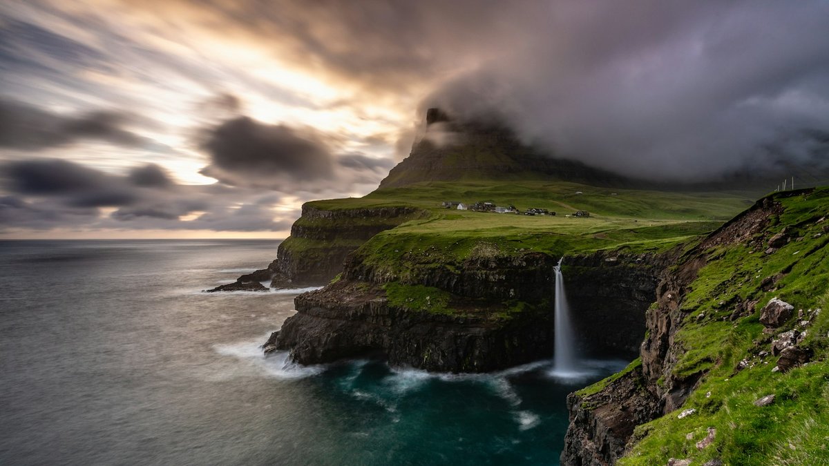 Múlafossur waterfall dropping from a grassy cliff towards the North Atlantic beside the village of Gásadalur