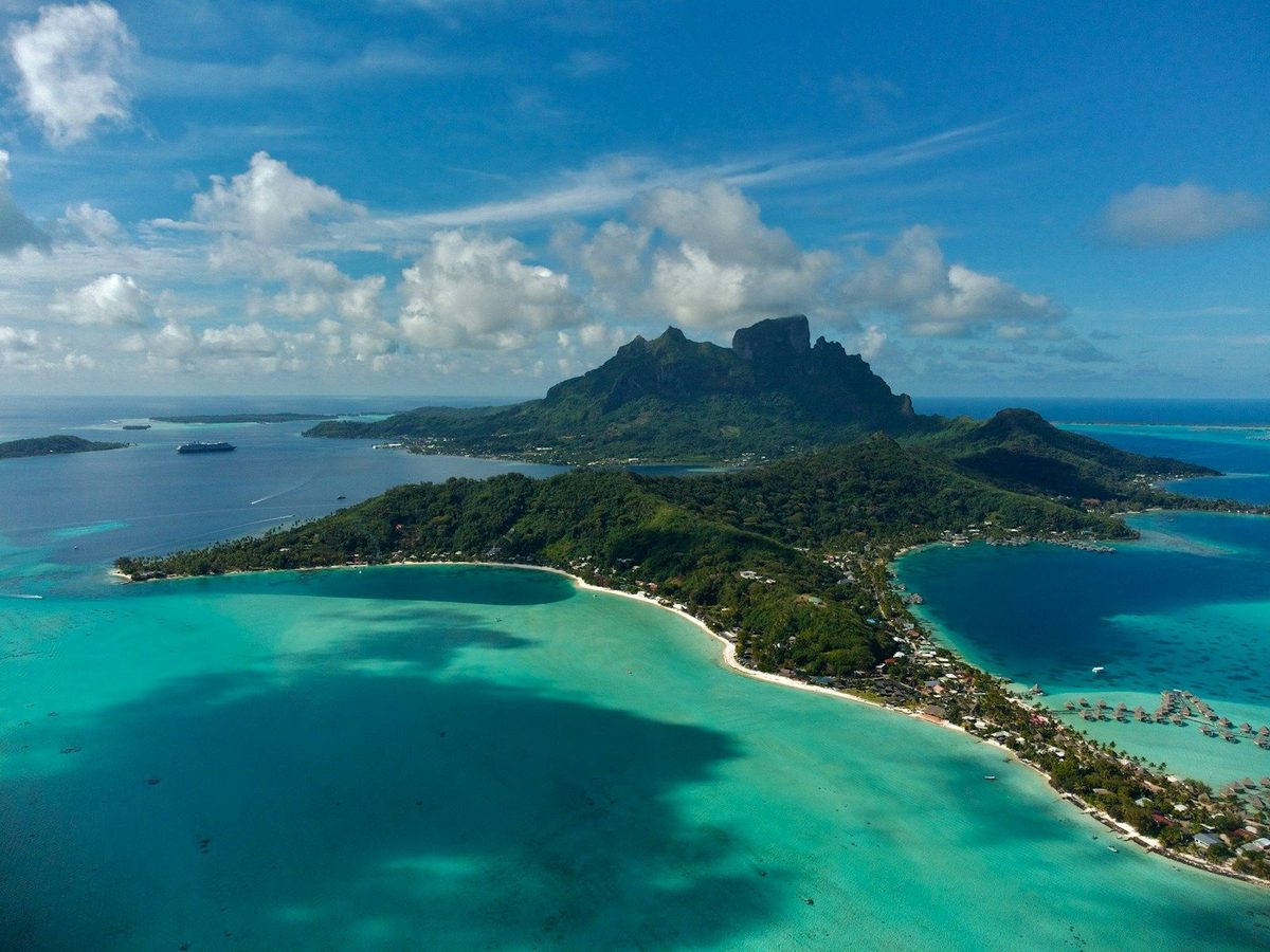 Aerial view of a turquoise South Pacific lagoon and reef around a green volcanic island in French Polynesia