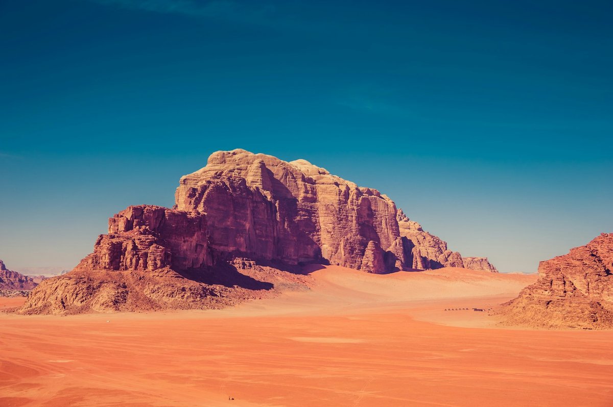 Sandstone rock formations rising from red-orange sand dunes in Wadi Rum, Jordan