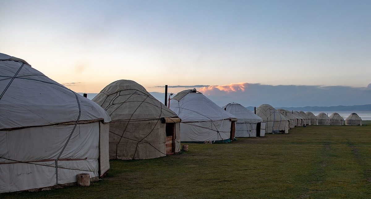 Traditional white yurts set against broad alpine grasslands and distant mountain ridges at Song-Kol, Kyrgyzstan