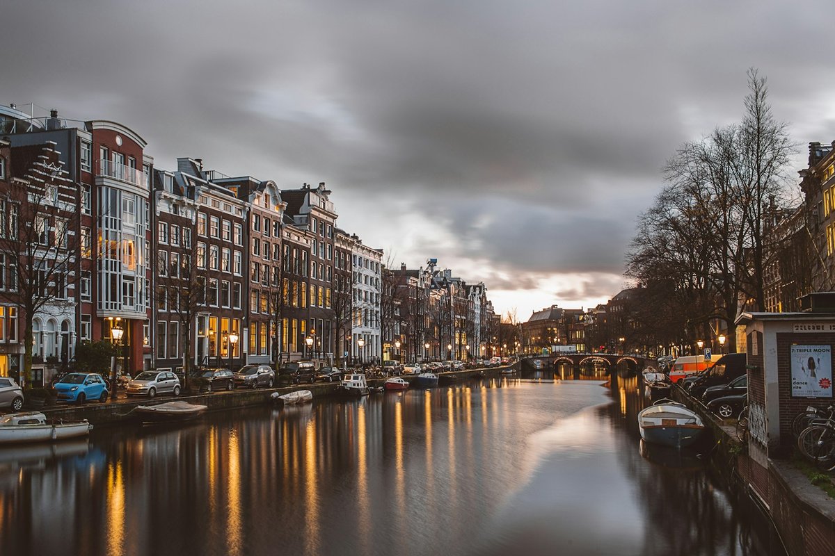 Amsterdam canal at dusk with canal houses, parked cars and a bridge in the distance
