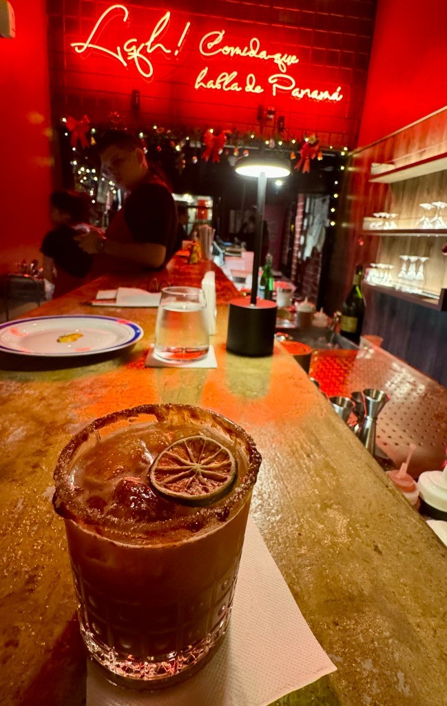 Tamarind mezcal margarita with a dried lime wheel on the bar at Fonda Lo Que Hay under a red neon sign reading Comida que habla de Panamá
