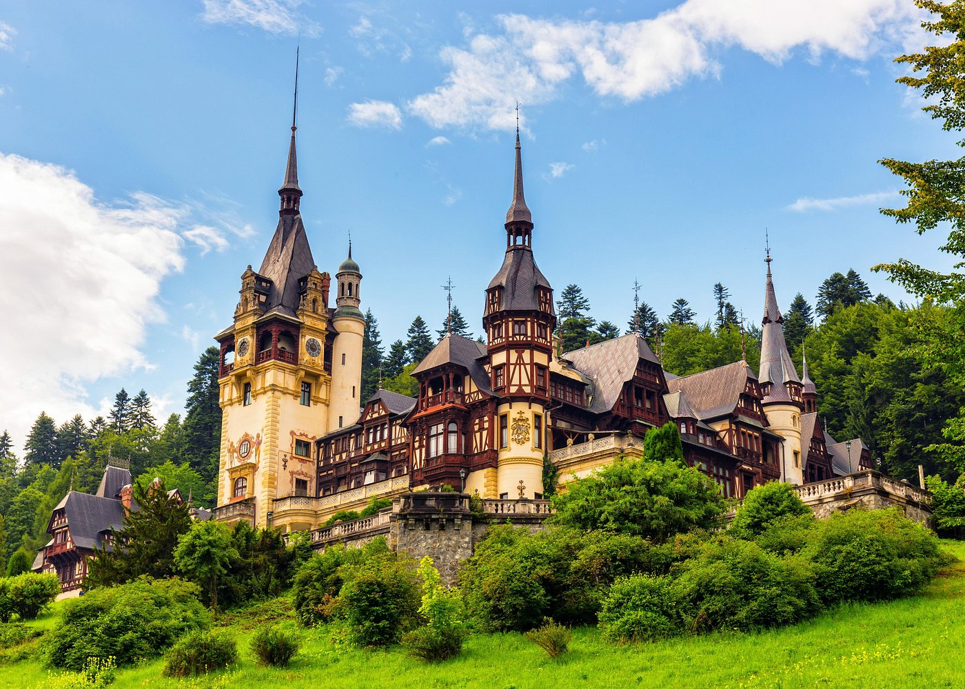 Peleș Castle's ornate towers and timber-framed façade rising above a green hillside